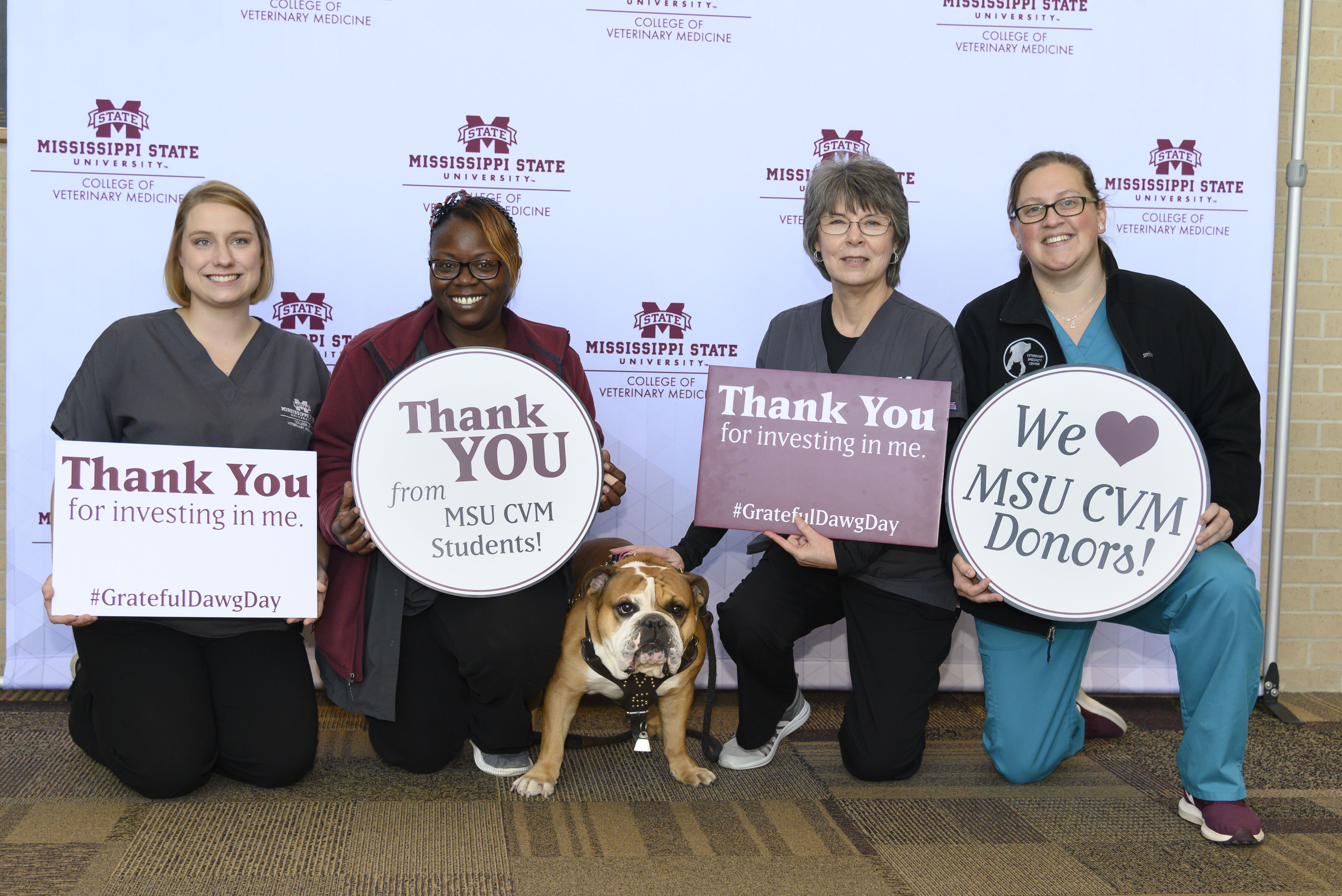 Four people pose with thank you signs and a bulldog